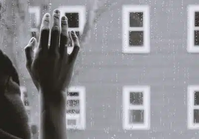 A woman's hand resting against a windowpane suggests grief. In counselling, the dual process model of grief states that both denying and avoiding are important parts of a healthy grieving process.