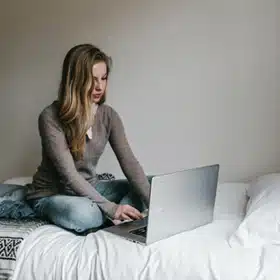 What is Online Counselling and Psychotherapy? - A woman typing on her laptop in bed. With email counselling, a person can receive help without leaving their home
